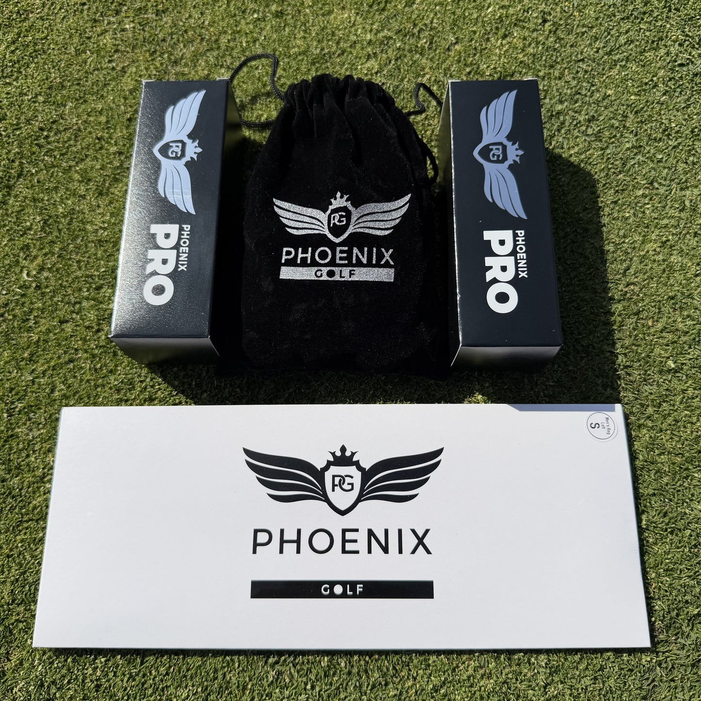 "Phoenix Pro Golf Sample Pack laid out on grass, featuring two sleeves of premium golf balls, one golf glove, and a bag of tees."