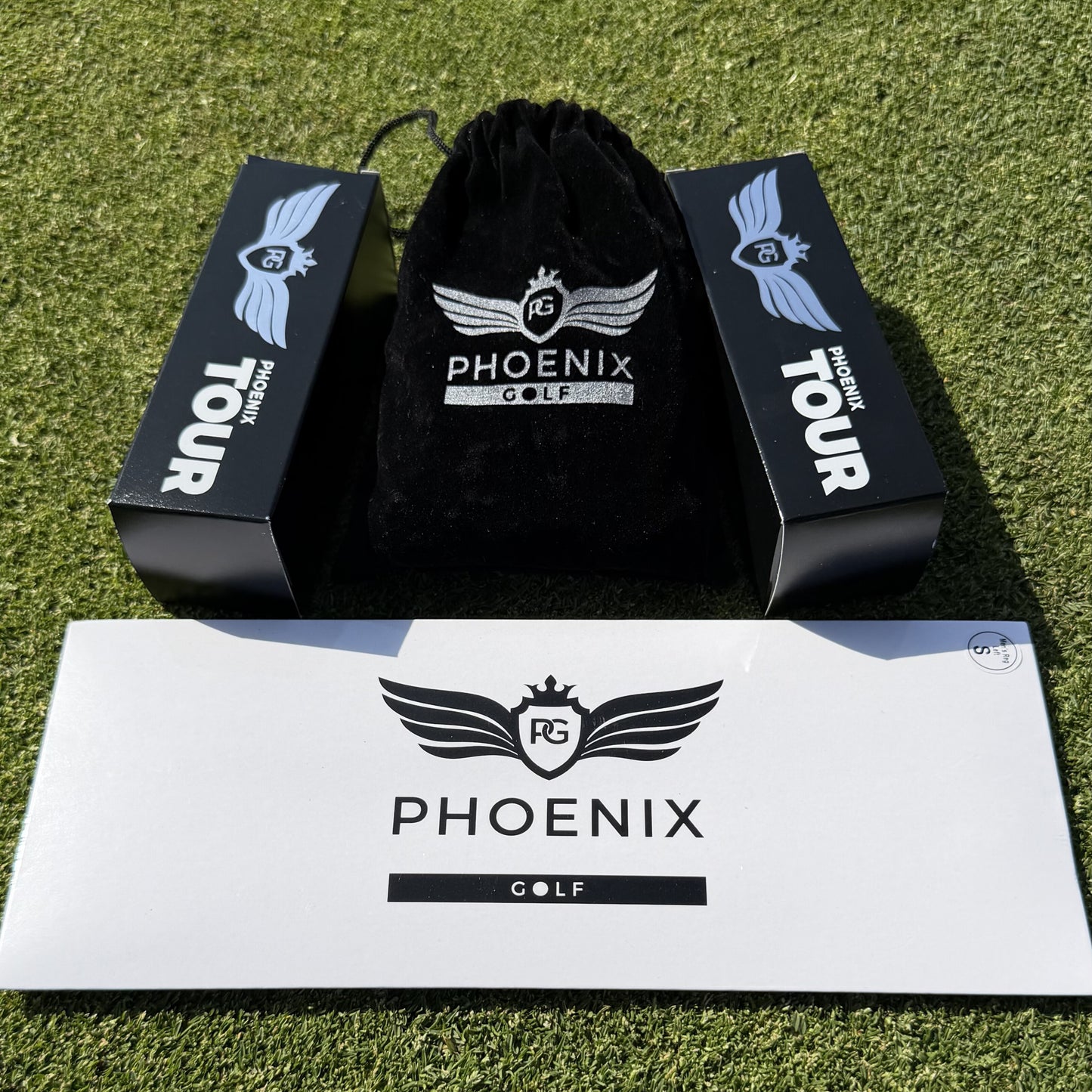 "Phoenix Tour Golf Sample Pack laid out on grass, featuring two sleeves of premium golf balls, one golf glove, and a bag of tees."