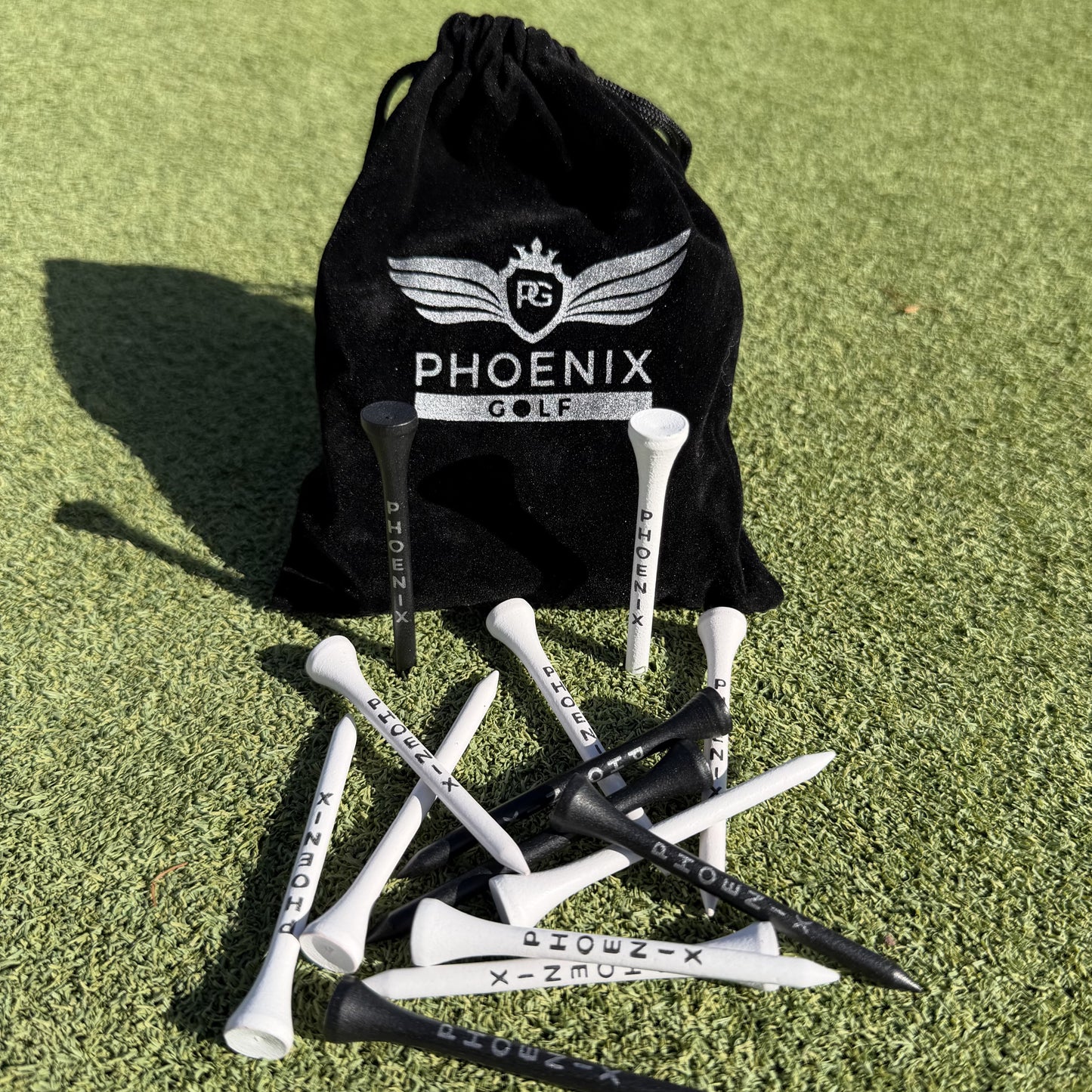 Phoenix Golf Pro Bamboo Golf Tees in black and white played on the floor, and a black velvet pouch with Phoenix golf branding on in silver.